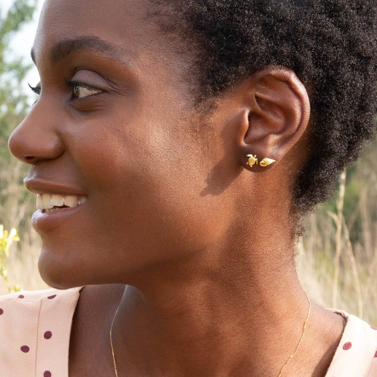 Woman wearing gold earrings outdoors with a blurred natural background